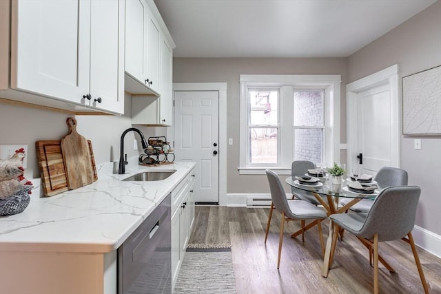 kitchen featuring stainless steel dishwasher, sink, hardwood / wood-style flooring, white cabinetry, and light stone counters