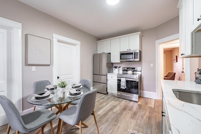 kitchen featuring light stone countertops, appliances with stainless steel finishes, white cabinetry, light wood-type flooring, and sink