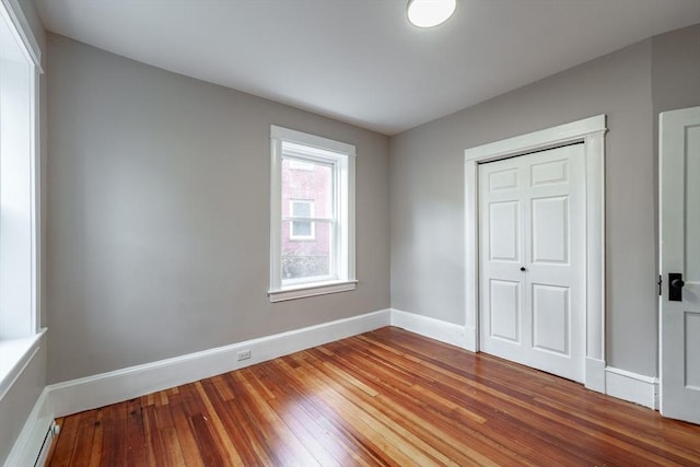 unfurnished bedroom with hardwood / wood-style flooring, baseboard heating, and a closet