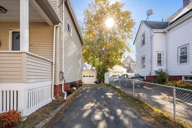 view of home's exterior featuring driveway, a detached garage, an outdoor structure, and fence