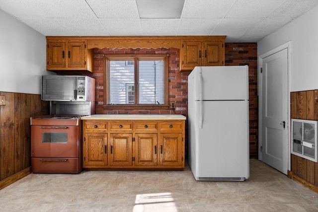 kitchen featuring stainless steel microwave, gas range, wooden walls, and freestanding refrigerator