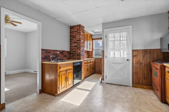 kitchen featuring wooden walls, range with gas cooktop, dishwasher, light countertops, and wainscoting