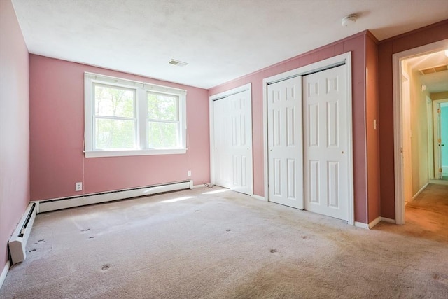 unfurnished bedroom featuring baseboard heating, two closets, carpet, and baseboards