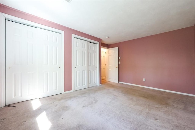 unfurnished bedroom featuring two closets, carpet, and baseboards