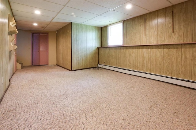 unfurnished room featuring a baseboard radiator, light carpet, wood walls, recessed lighting, and a drop ceiling