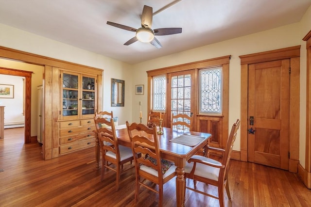 dining space with a baseboard heating unit, a ceiling fan, and wood finished floors