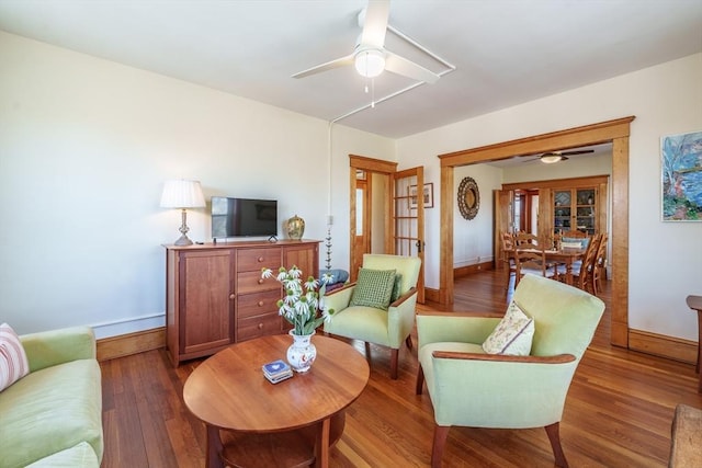 living room featuring a ceiling fan, baseboards, and wood finished floors