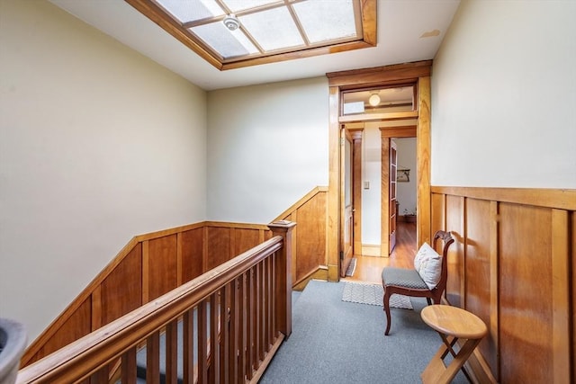 hall featuring light carpet, a wainscoted wall, wooden walls, and an upstairs landing