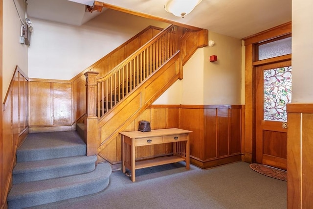 stairway with a wainscoted wall, wood walls, and carpet flooring