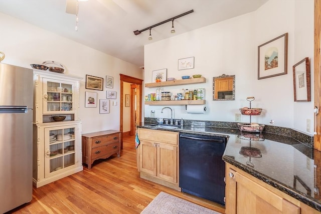 kitchen with black dishwasher, light wood-style flooring, freestanding refrigerator, a sink, and dark stone counters