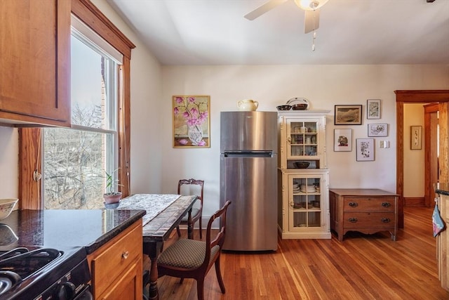 kitchen featuring brown cabinetry, a ceiling fan, dark countertops, light wood-style flooring, and freestanding refrigerator