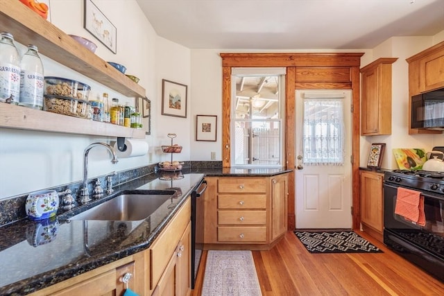 kitchen featuring brown cabinets, light wood-style floors, a sink, dark stone countertops, and black appliances