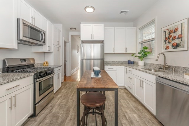 kitchen featuring light wood-type flooring, light stone countertops, stainless steel appliances, and white cabinets