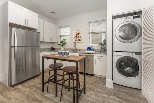 laundry area featuring stacked washer / drying machine, hardwood / wood-style flooring, and sink