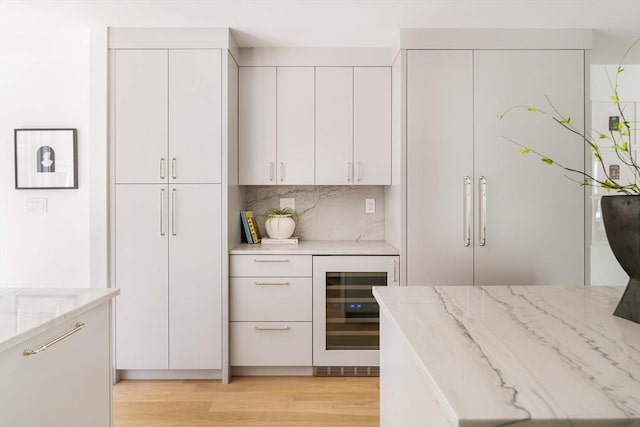 13 Mellen St, Cambridge, MA 02138 - kitchen featuring wine cooler, light stone counters, white cabinetry, light wood-style floors, and backsplash