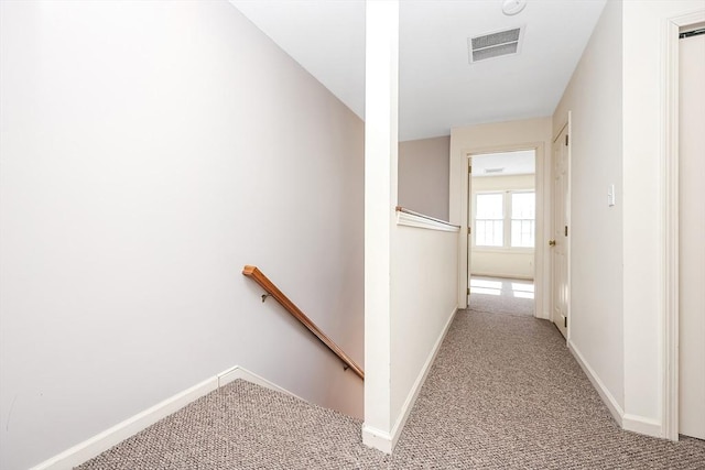 hall featuring baseboards, an upstairs landing, visible vents, and light colored carpet