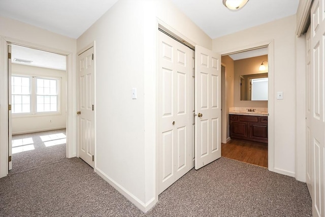 hall with carpet floors, a sink, visible vents, and baseboards