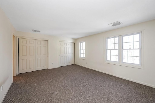 unfurnished bedroom with dark colored carpet, two closets, and visible vents