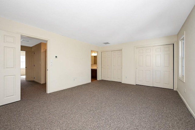 unfurnished bedroom with baseboards, dark colored carpet, visible vents, and multiple closets