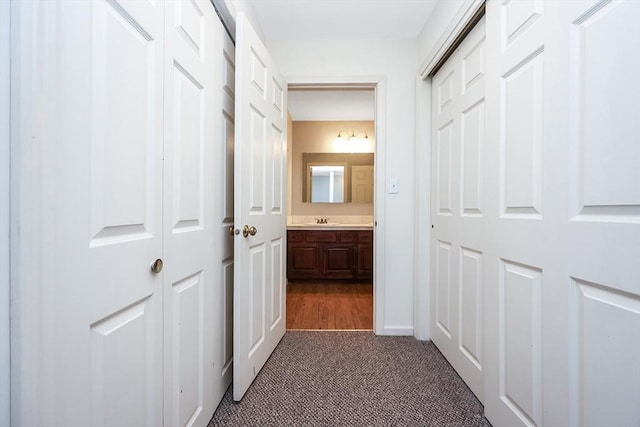 hallway with dark colored carpet and a sink