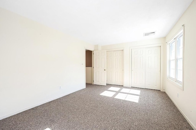 unfurnished bedroom with carpet floors, visible vents, baseboards, and two closets