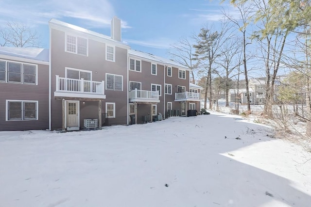 snow covered back of property featuring central AC and a chimney