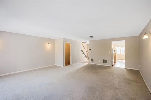 unfurnished living room with light carpet, visible vents, stairway, and baseboards