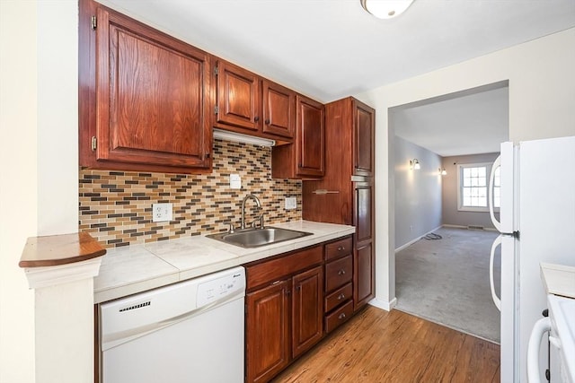 kitchen with white appliances, tile counters, decorative backsplash, light wood-type flooring, and a sink