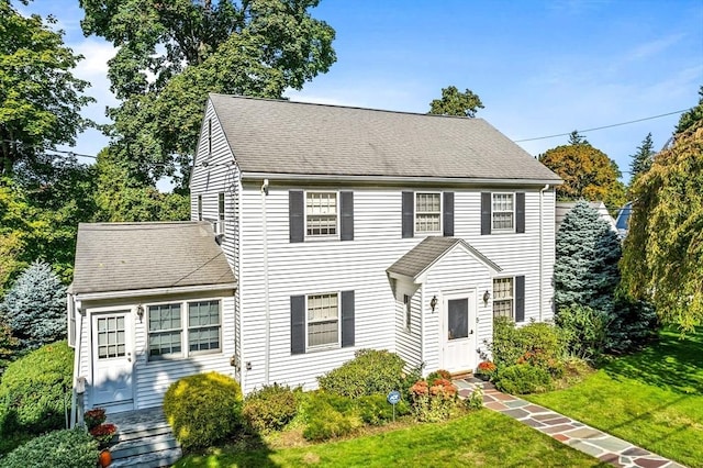 colonial inspired home with entry steps, a shingled roof, and a front lawn