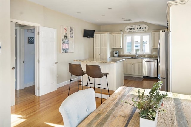 kitchen featuring light stone countertops, light wood-type flooring, stainless steel appliances, a kitchen island, and a breakfast bar area