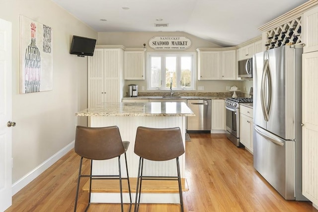 kitchen featuring light stone countertops, appliances with stainless steel finishes, sink, light hardwood / wood-style flooring, and a center island