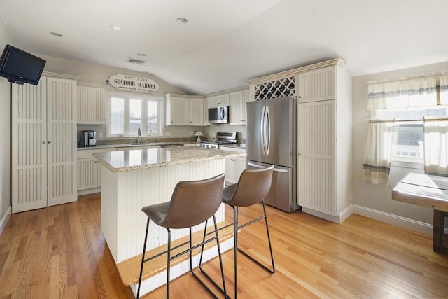 kitchen with lofted ceiling, light hardwood / wood-style flooring, appliances with stainless steel finishes, a kitchen island, and white cabinetry