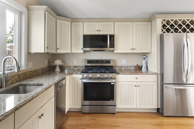 kitchen with stainless steel appliances, sink, cream cabinets, stone counters, and light hardwood / wood-style floors