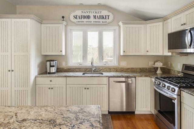 kitchen with appliances with stainless steel finishes, light stone counters, dark wood-type flooring, sink, and lofted ceiling