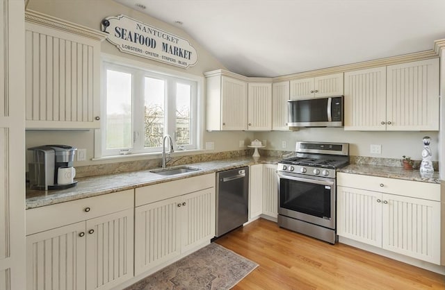 kitchen with cream cabinets, sink, vaulted ceiling, light wood-type flooring, and stainless steel appliances