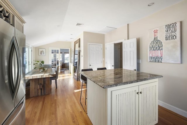 kitchen featuring stainless steel refrigerator, a center island, light hardwood / wood-style flooring, dark stone countertops, and a breakfast bar