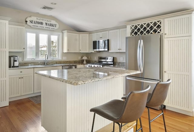 kitchen featuring a center island, lofted ceiling, sink, appliances with stainless steel finishes, and a breakfast bar area