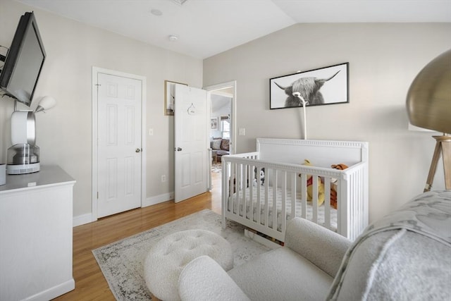 bedroom with a crib, hardwood / wood-style floors, and lofted ceiling