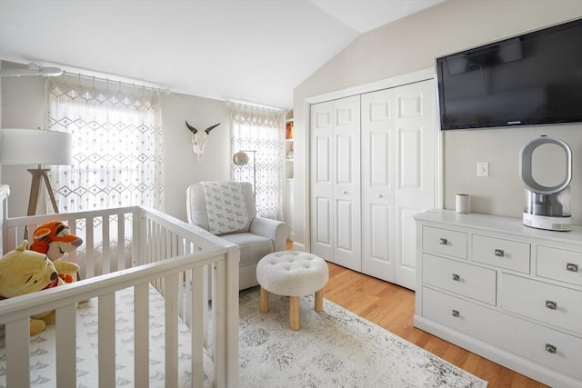 bedroom featuring a closet, light hardwood / wood-style flooring, a nursery area, and lofted ceiling