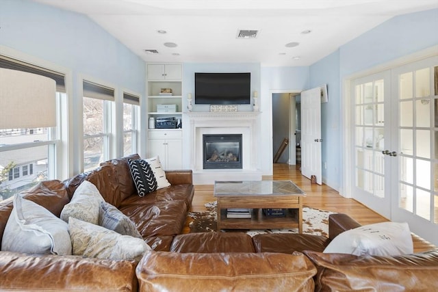 living room with built in features, french doors, light hardwood / wood-style floors, and lofted ceiling