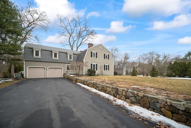 colonial inspired home with a garage, driveway, a chimney, and a gambrel roof