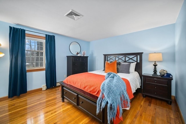 bedroom featuring a baseboard heating unit, light wood finished floors, visible vents, and baseboards