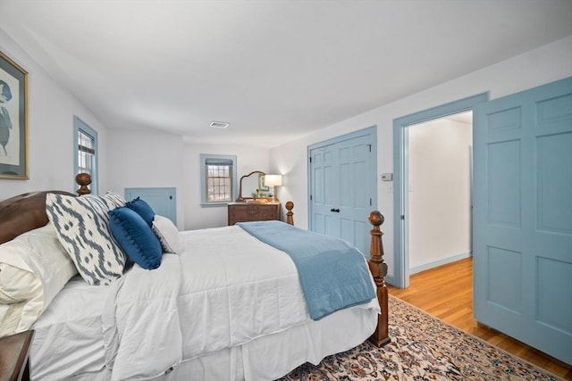 bedroom with wood finished floors, visible vents, and baseboards