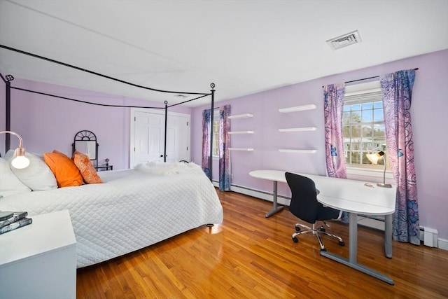 bedroom with a baseboard radiator, visible vents, baseboards, and wood finished floors