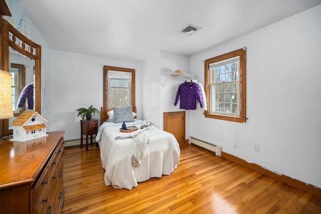 bedroom featuring light wood-style floors, visible vents, and a baseboard heating unit