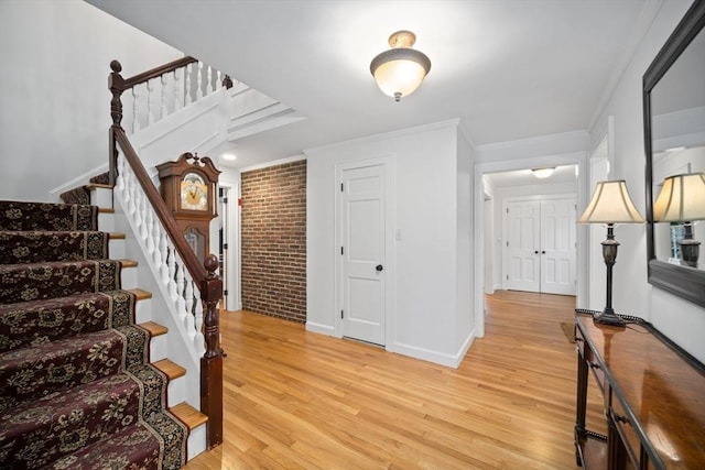 entrance foyer featuring light wood-type flooring, brick wall, and ornamental molding