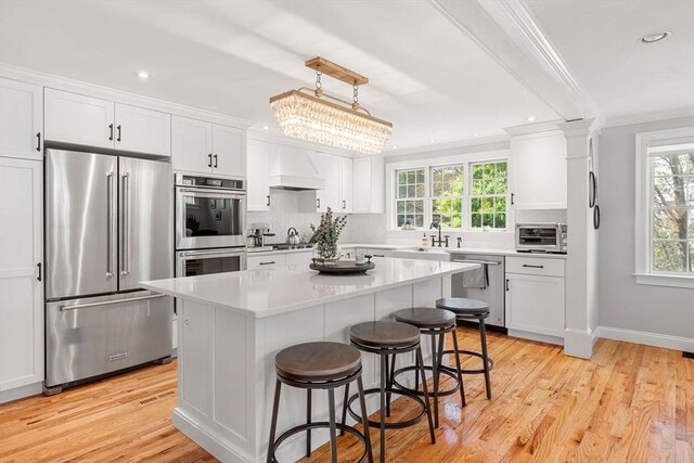 37-1/2 Federal St, Newburyport, MA 01950 - kitchen with appliances with stainless steel finishes, crown molding, white cabinets, decorative backsplash, and a breakfast bar