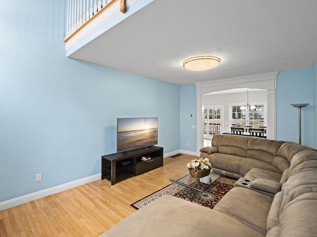 living room featuring a chandelier, arched walkways, baseboards, and wood finished floors