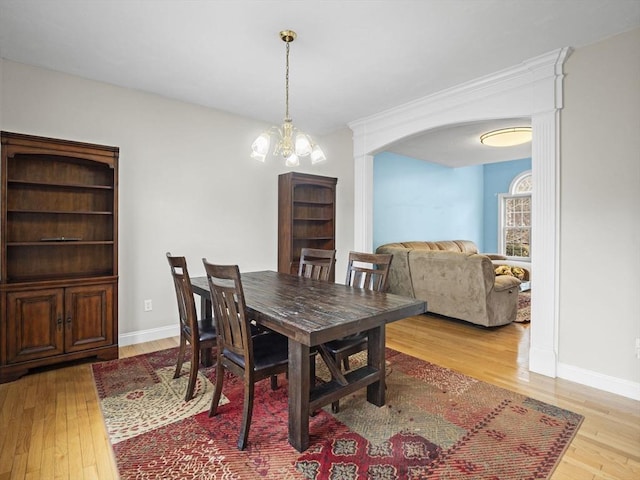 dining area featuring baseboards, hardwood / wood-style floors, arched walkways, and an inviting chandelier