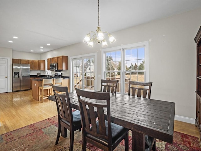 dining space featuring light wood finished floors, baseboards, a notable chandelier, and recessed lighting